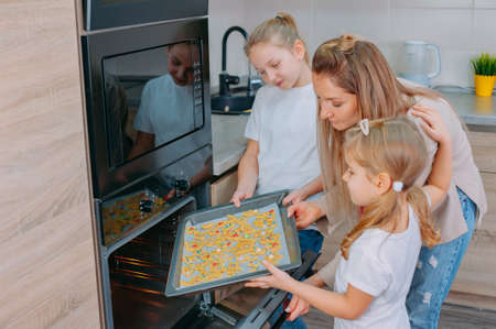 Mom teaches her daughters to cook in the kitchen. The family bakes cookies in the ovenの写真素材