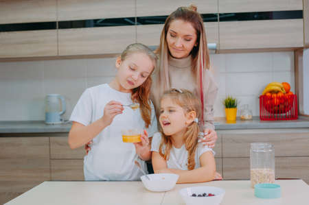 A mom and her two daughters add honey to oatmeal in the kitchenの写真素材