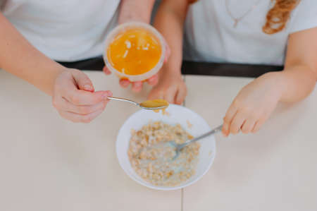 Two sisters add honey to oatmeal in the kitchenの写真素材