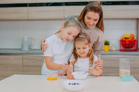 A mom and her two daughters add honey to oatmeal in the kitchenの写真素材