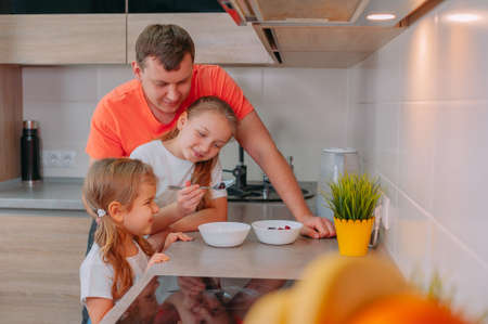 A father feeds his daughters in the kitchen on a background of fruitsの写真素材