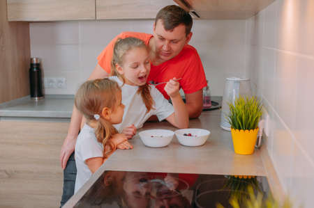 A father feeds his daughters in the kitchen on a background of fruitsの写真素材