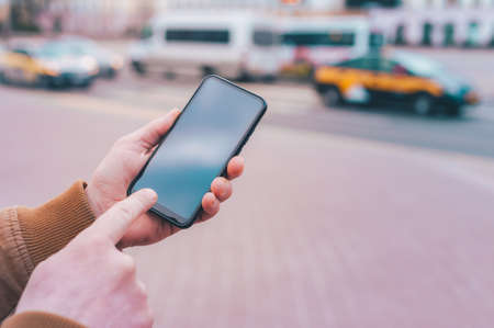 A man holds a mock-up of a smartphone on the background of the roadの写真素材