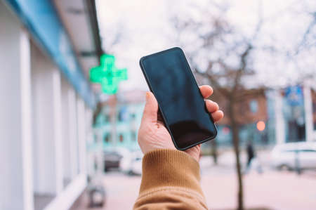A man holds a mock-up of a smartphone on the background of a pharmacy in the cityの写真素材