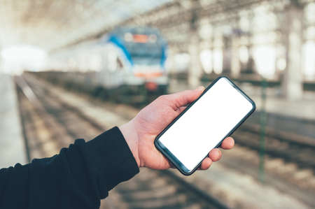 A man holds a mock-up of a smartphone on the background of a train at a railway stationの写真素材