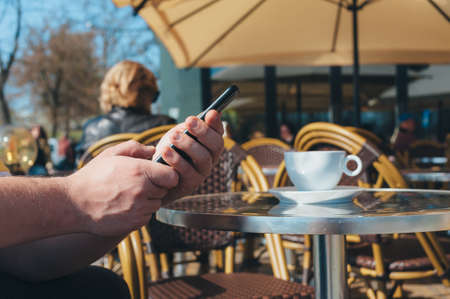 Man holds a smartphone on the background of a cup of coffee in a restaurantの写真素材