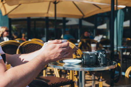 Photographer man drinks coffee in a restaurant on the background of a table with a cameraの写真素材