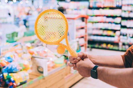 A man in a store selects a children's tennis set and holds a tennis racket in his handsの写真素材