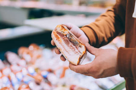 A man in a store holds smoked bacon in his handsの写真素材