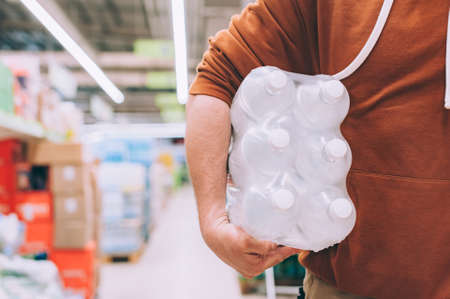 A man in a store holds a package of clean and transparent bottled waterの写真素材