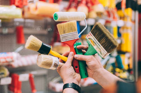 A man in a hardware store holds a set of brushes and rollers for paint and decorの写真素材