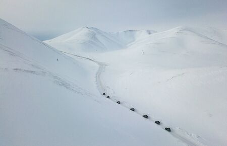 An elevated aerial view at the white mountains with lonely convoy of cars making their way through itの写真素材