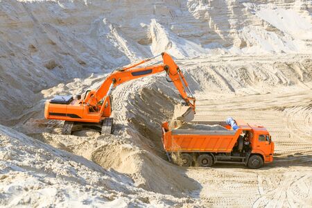 Excavator loading dumper truck with sand at a sand quarry