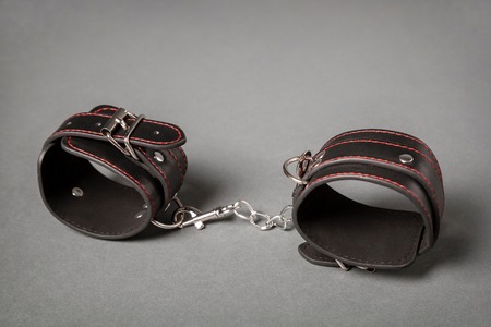 Black leather handcuffs on gray background. Sex toy.