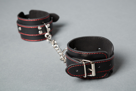 Black leather handcuffs on gray background. Sex toy.