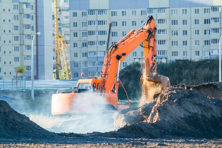 Orange excavator digging the ground at the construction site.