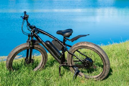 Black electric bike with thick wheels on the grass near the lake. Fatbike.