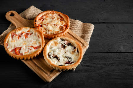 Three small pizzas on a cutting board on a black wooden background. With a copy space.の写真素材