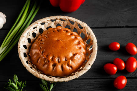 Round pie in a wicker basket on a black wooden background. composition with ingredients.の写真素材