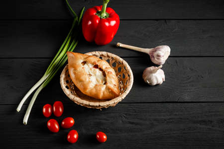 Pie in a wicker basket on a black wooden background. With a copy space.Vegetable composition - tomatoes, pepper, onion, garlic.の写真素材