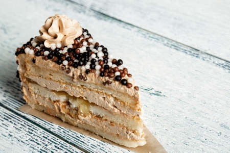 Piece of cake with cream and sweet balls on a white wooden background.