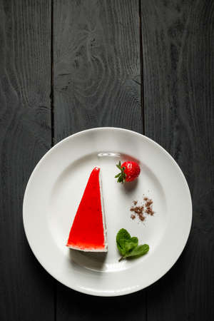 Strawberry cheesecake on a white plate. Black wooden background with a copy of the space.の写真素材