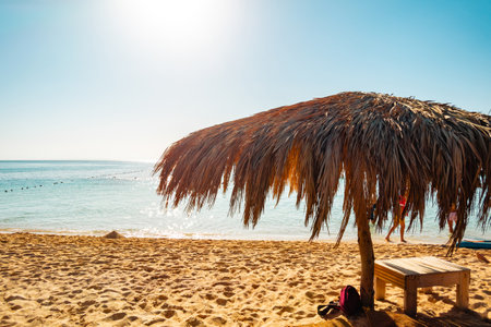Tropical beach umbrella on the background of the blue sea and sky. The roof is made of dried palm branches. The concept of tourism and travel.の写真素材
