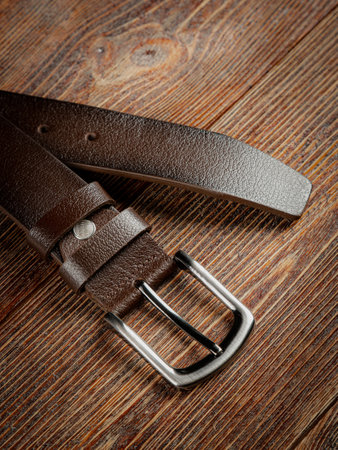 Brown leather belt on a wooden brown background. Close-up.