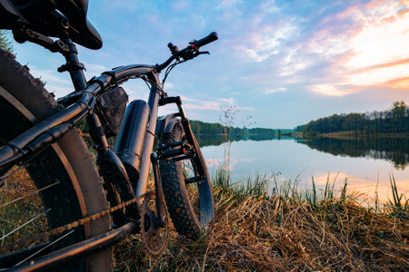 Electric bike with thick wheels on the background of lake and sunset. Sports fatbike. Picturesque place in the village. The concept of a healthy lifestyle.の写真素材