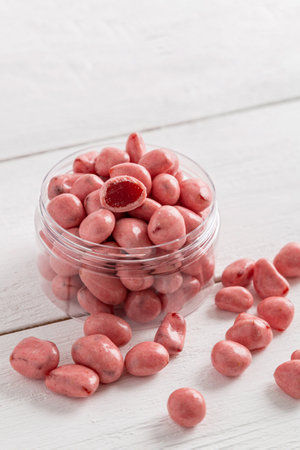 Dried fruits and berries in chocolate glaze. Pink candies on a white wooden background.