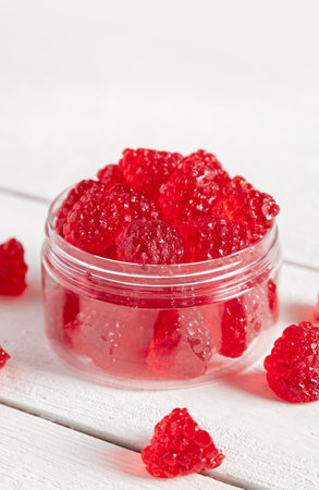 Raspberry shaped candies in a glass jar. White wooden background.