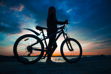 Young woman with the bicycle at sunset silhouetteの写真素材