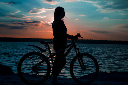 Young woman with the bicycle at sunset silhouetteの写真素材