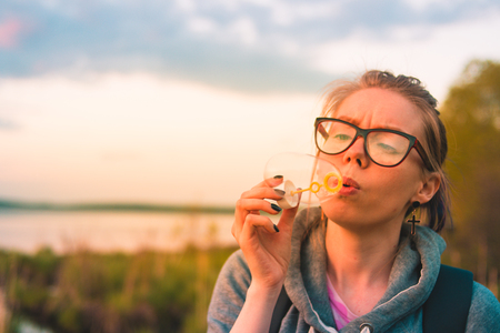 Girl blowing bubbles near the lake at sunsetの写真素材