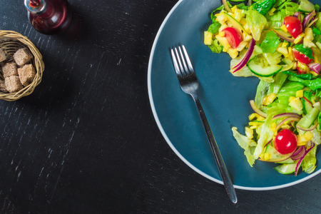 Blue plate of salad with mango, cucumber and cherry tomatoes on black table top viewの写真素材