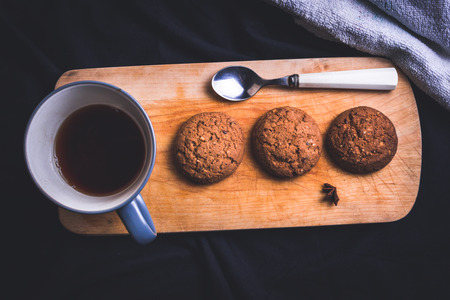 Cup of tea with oatmeal cookies and spoon on the wooden board top view