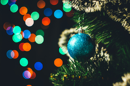Blue Christmas ball on the spruce Christmas tree with multicolored bokeh round garland lights backgroundの写真素材