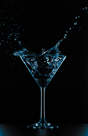 Cocktail martini glass liquid splash on black backgroundの写真素材