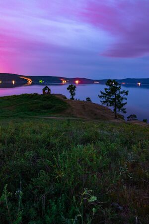 Beautiful long exposure landscape view of the mountain lake Turgoyak, Russia with purple sky and summer house on the hill in summer nightの写真素材