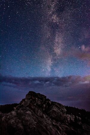 Milky Way galaxy in the night sky above rocky mountain and stormy clouds