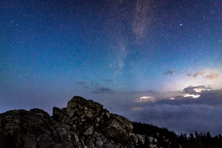 Milky Way galaxy in the night sky above rocky mountain and stormy cloudsの写真素材