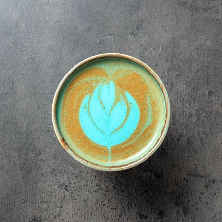 Close up of turquoise colored capuccino in beautiful greenish-blue cup with latte art on concrete gray background top viewの写真素材