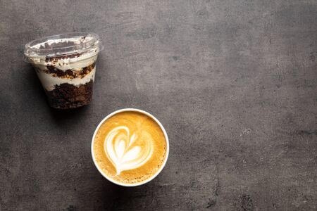 Dessert in plastic container and cup of cappuccino to go top view on grey background