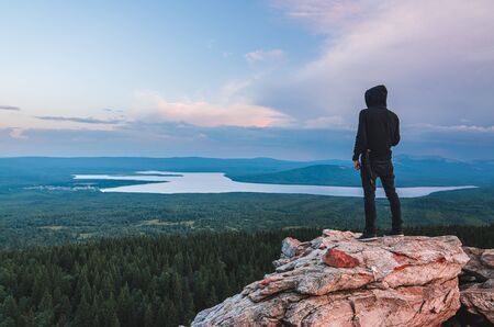 A lonely man standing on the rock at the top of Zyuratkul National Park mountains looking at the valley and lakeの写真素材