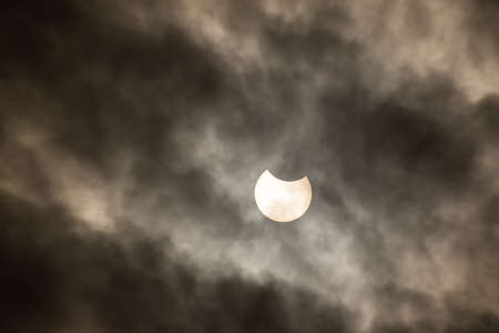 A phase of solar eclipse with sun disc behind the clouds. High quality photo