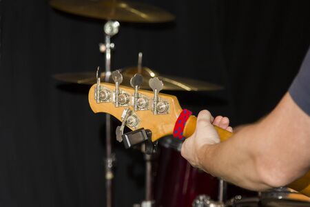 Fretboard of a five string bass guitar with a musician's hand on the background of a drum kit in the Studio.の写真素材