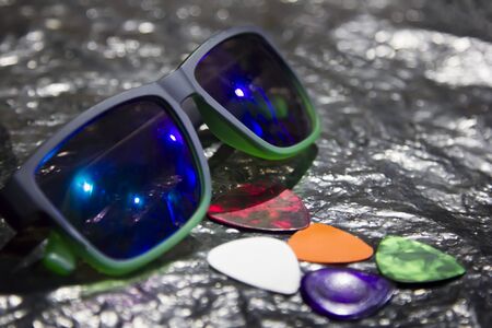 A composition of glasses and guitar picks lying on a metal surface.の写真素材