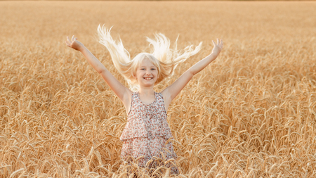Little girl is playing with her hair in a field with wheatの写真素材