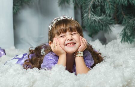Little girl lying in the snow and smiling at the background of a fur-tree, photosession Studios. new year2018, Christmas decorationの写真素材