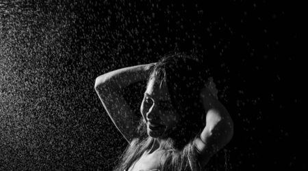 Happy girl portrait and splashing water in her face. beautiful female model on black background.